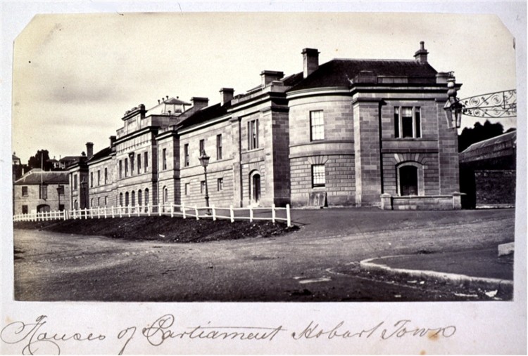 Two storey sandstone Parliament House building in Hobart, with unsealed road in foreground. Location hand inscribed beneath.